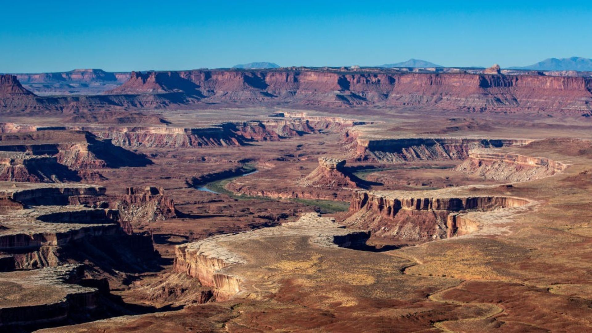 An aerial view of a winding canyon with steep walls and a meandering river flowing through it. Mountains rise in the background