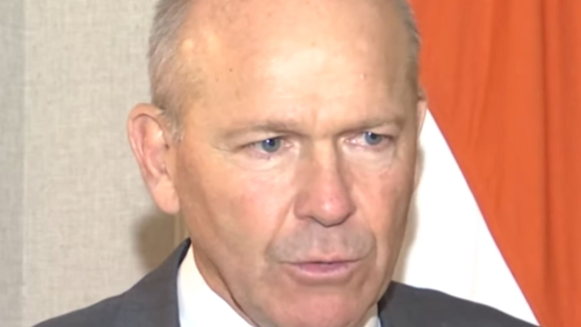 Close-up image of Dave Calhoun with a portion of an orange curtain in the background
