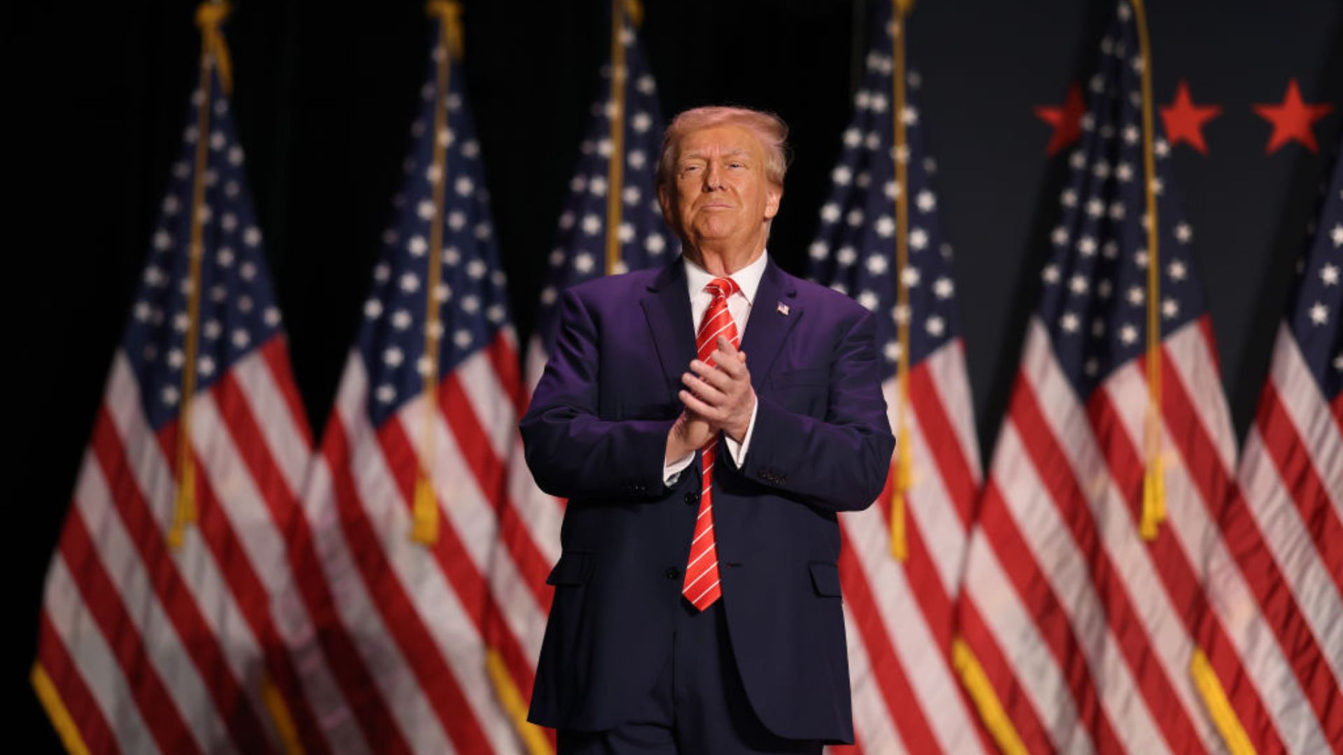 Donald Trump stands against a backdrop of multiple American flags
