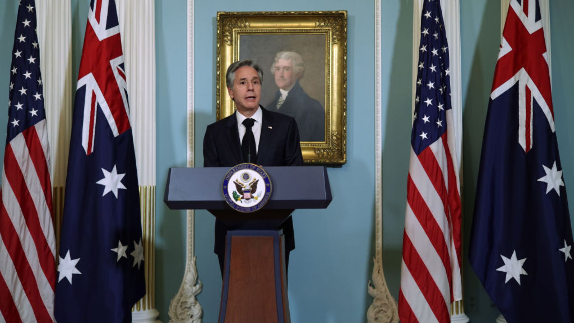 Antony Blinken in a suit speaking at a podium with the seal of the United States