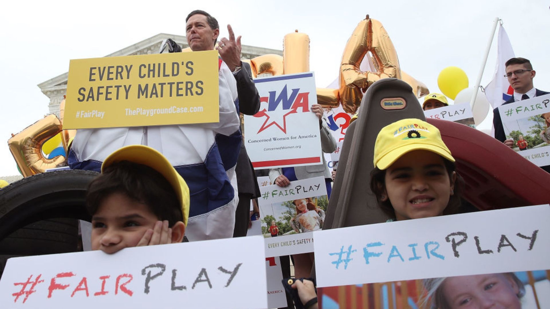People gathered for a demonstration, holding signs with messages emphasizing children's safety. A prominent banner reads "EVERY CHILD'S SAFETY MATTERS" with the hashtag "#FairPlay" and a website reference "ThePlaygroundCase.com"
