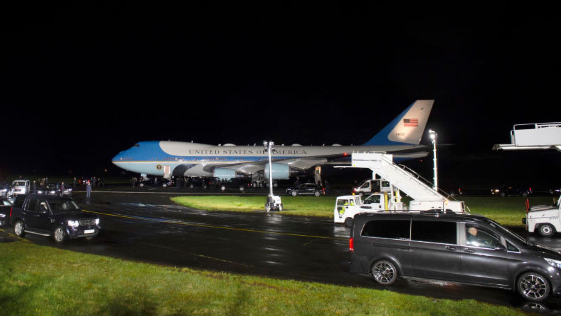 Nighttime scene of the Air Force One aircraft with "UNITED STATES OF AMERICA" written on its side, parked on a tarmac