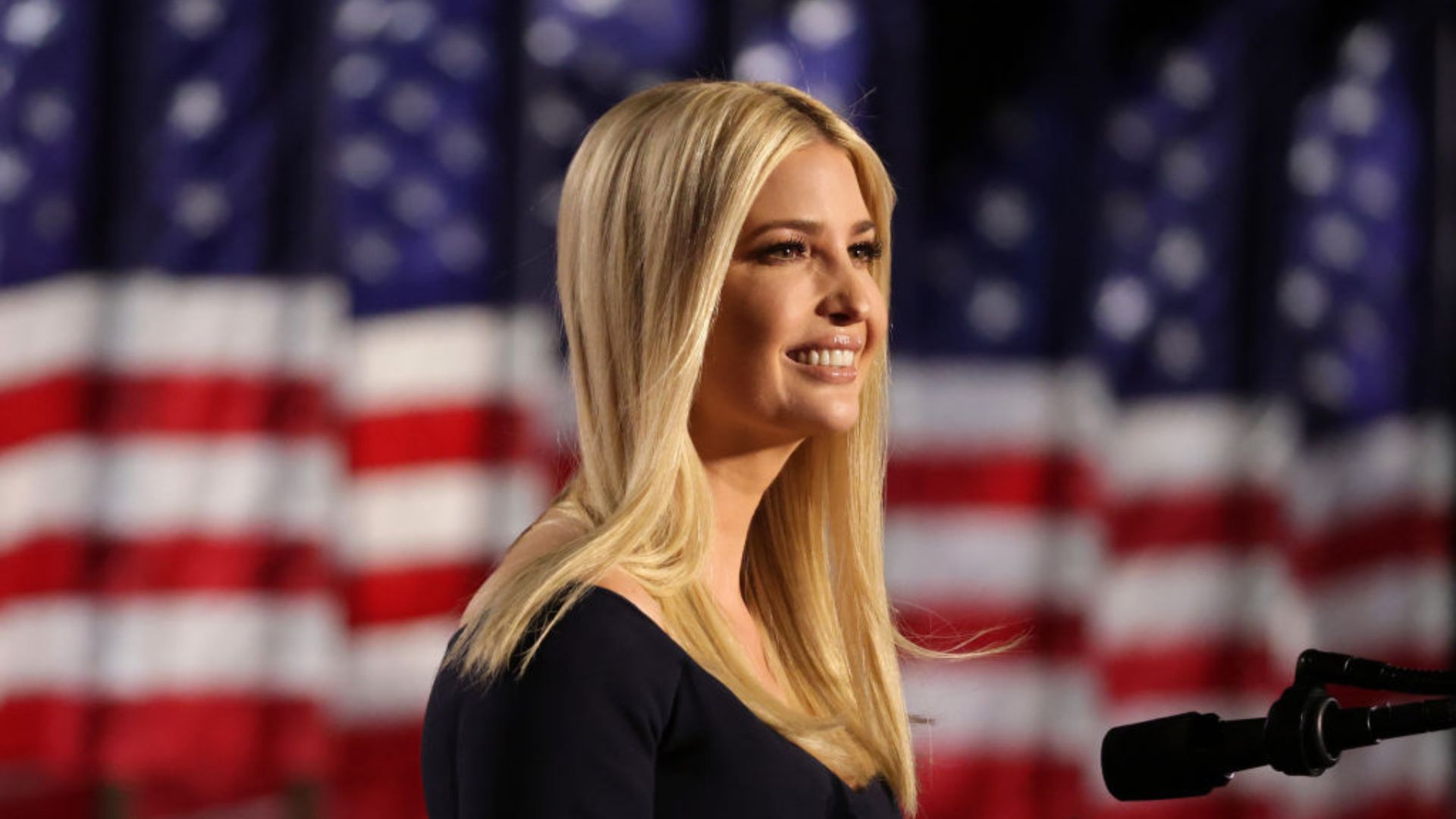Ivanka Trump smiles as she stands in front of a backdrop of American flags