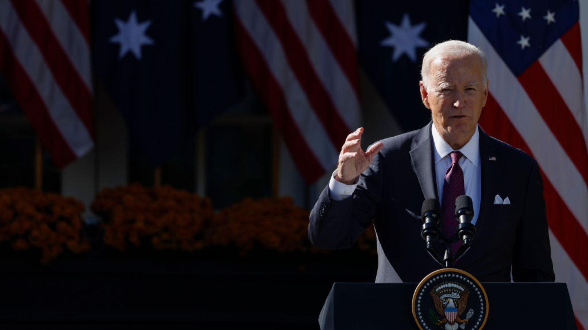 Joe Biden stands at a podium with the Presidential seal, addressing an audience