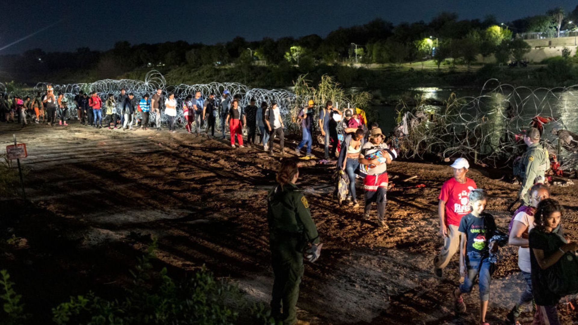 A group of people, including children and adults, gathered near a barbed wire fence at night