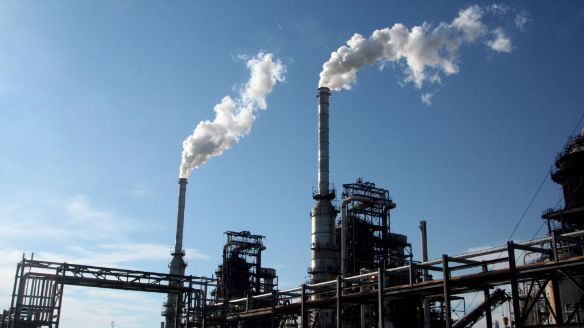 Industrial Plant Emissions Alt Text: An industrial plant with multiple tall chimneys emitting white smoke against a clear blue sky
