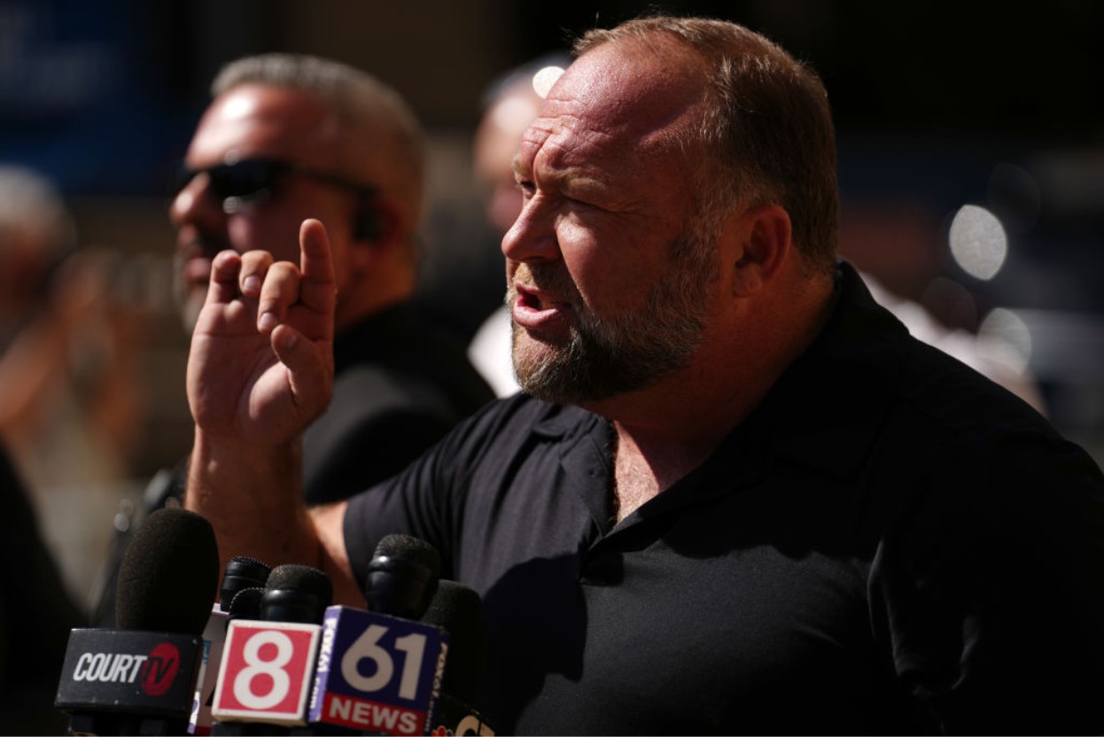 Alex Jones speaking aggressively into a microphone while speaking to the press
