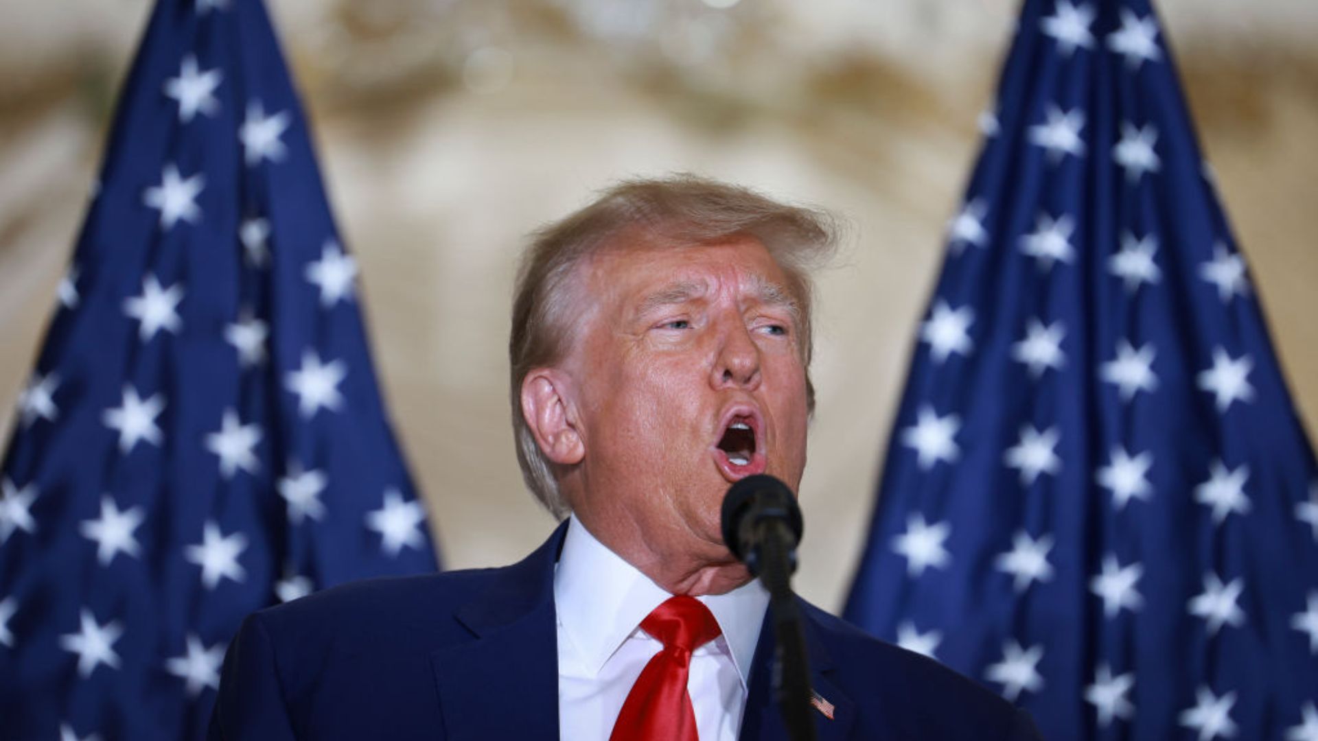 Donald Trump speaking into a microphone with American flags in the background