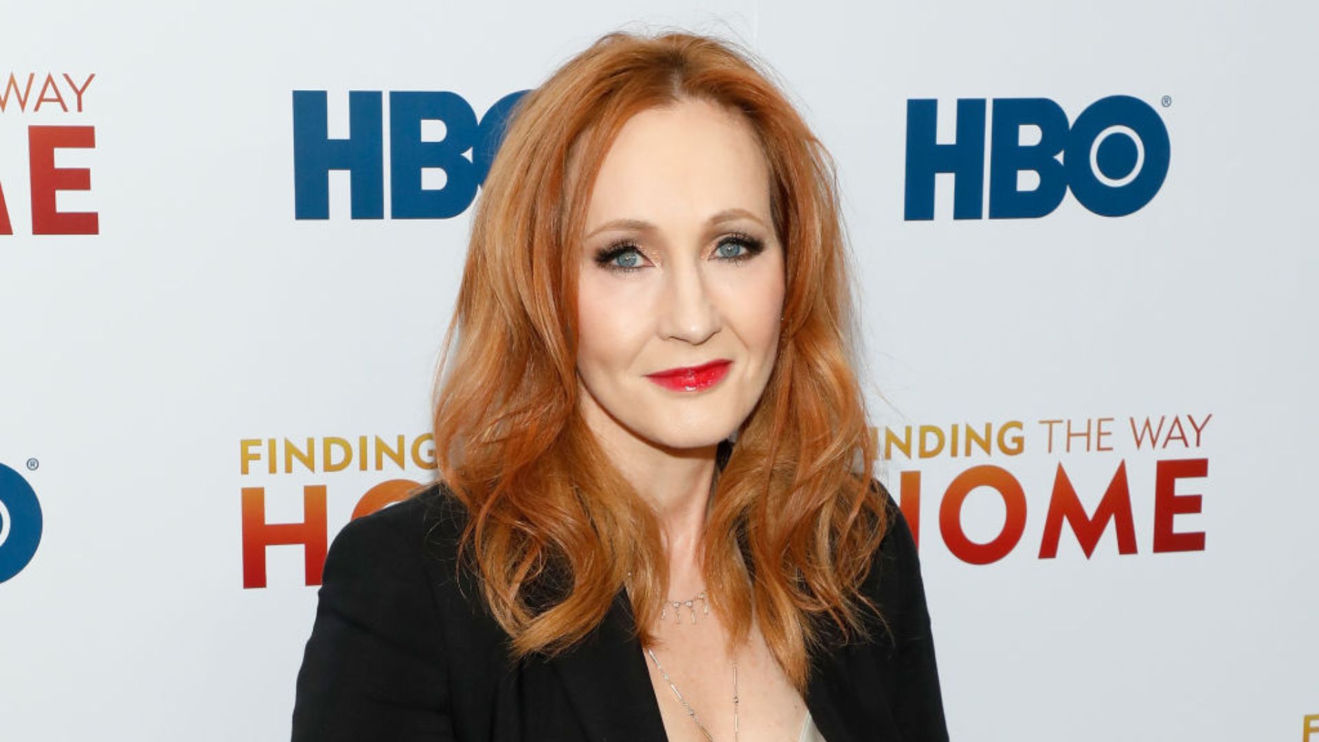 J.K. Rowling posing in front of a promotional backdrop at an HBO event